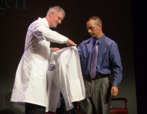 Dr. Stephen Meyers, medical director of the Department of Physician Studies at HPU, presents student Shane Georgeff with his white coat.