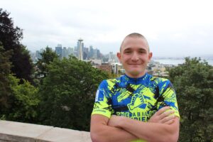 High Point University student Wayne Burger smiles while wearing his cycling uniform with the Seattle skyline in the background.