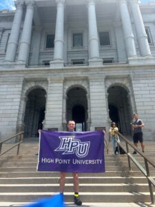 Wayne Burger held up a High Point University flag during a stop along his bike ride across the United States.