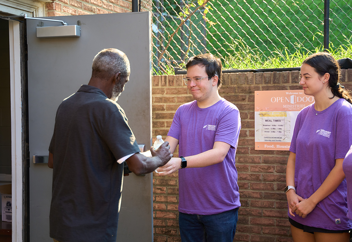 A local man accepts food and water from HPU pharmacy students Maxwell Crum and Lexie Soteriou during the day of service at Open Door Ministries. 