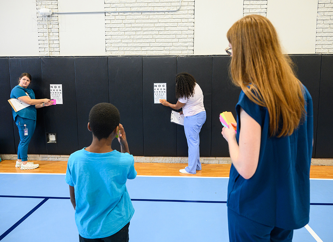 Ellie Abel, an HPU PA student from Middletown, Maryland, is pictured at front right screening a local boy while fellow PA students Sarah Beth Wells of Jonesborough, Tennessee, and Clara Primus of High Point, pointed to lines on visual acuity charts for children to read.