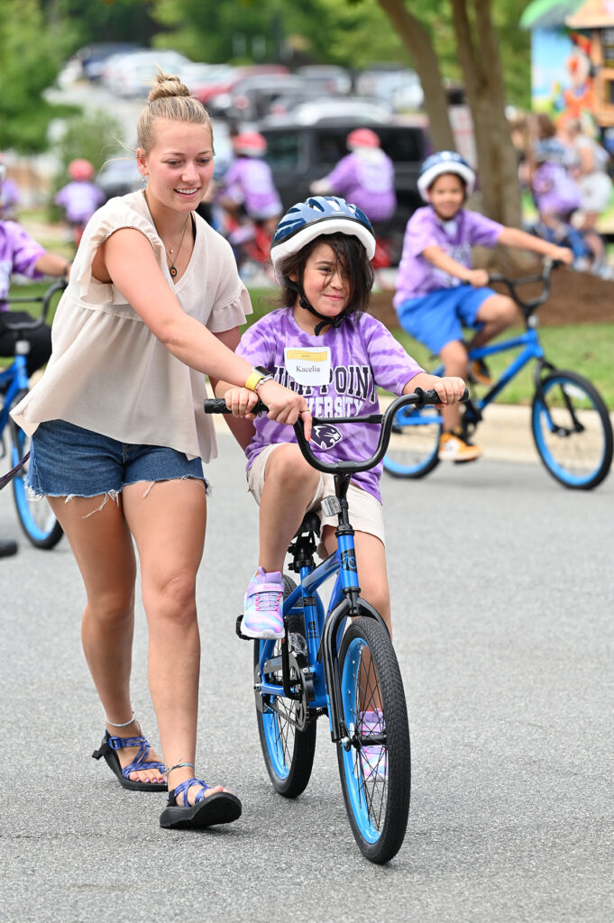 An HPU student helps a local child to ride her bike for the first time.